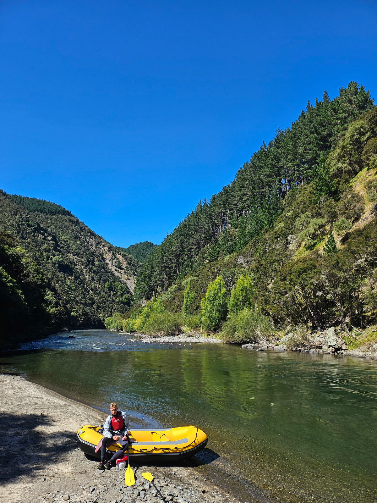 A kayaker paddling a clear river through a bush-clad gorge